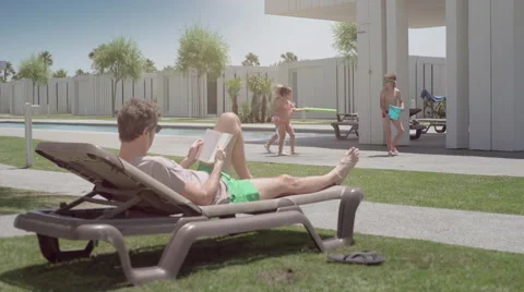 Man reading a book while child play in a resort Stock Footage 65216956