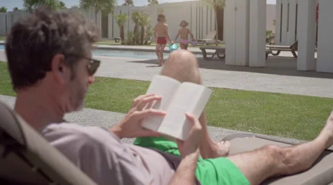 Man reading a book while child play in a resort Stock Footage 65217567