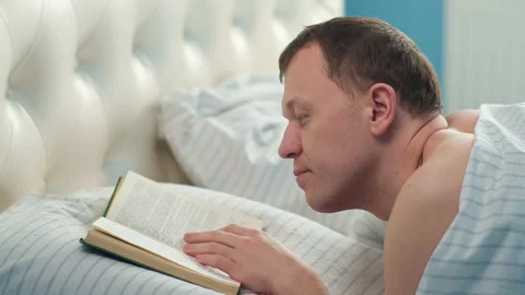 Man reading book while lying in bed in the morning, camera movement, relaxation Stock Footage 144351656