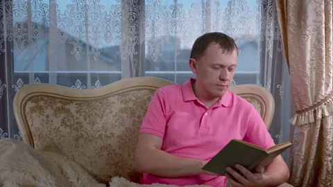 Man reading a book while sitting in the evening on the sofa, window background Stock Footage 153952881