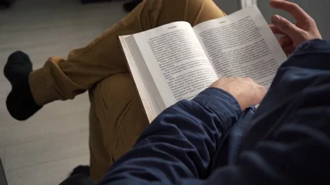 A man reading a book while sitting on a chair in the room Stock Footage 154503718