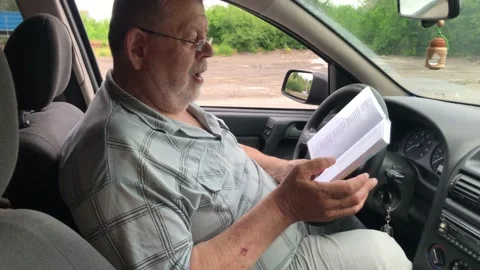 Man reading book while sitting inside of passenger car on driver seat Video stock 157177229