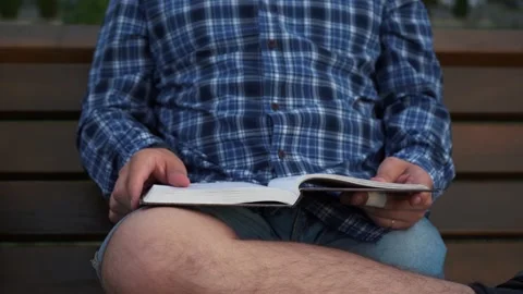 A man reading a book while sitting on a bench Stock Footage 157368208