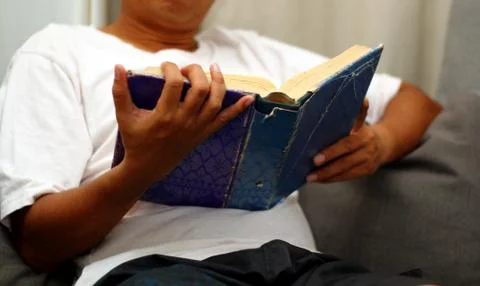 Man reading book while sitting on sofa Stock Photos