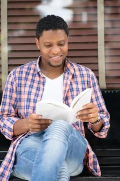 Man reading a book while sitting at a store window. Stock Photos