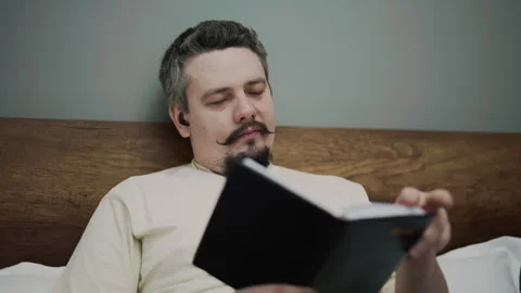 Man reading book with wireless earphones in bed Stock Footage 340926839