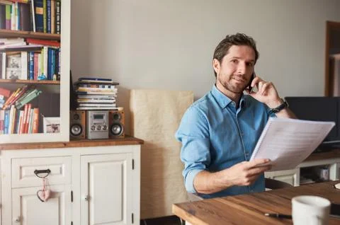 Man reading documents and talking on a cellphone at home Stock Photos