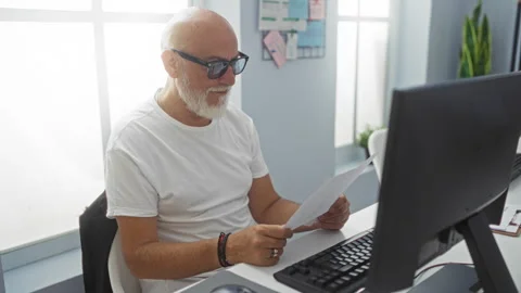 Man reading documents at a desk in a modern office with a computer screen a.. Stock Footage 279387683