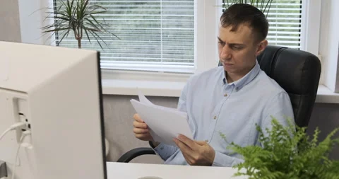 Man reading documents while sitting behind a computer monitor in office Stock Footage 164858244