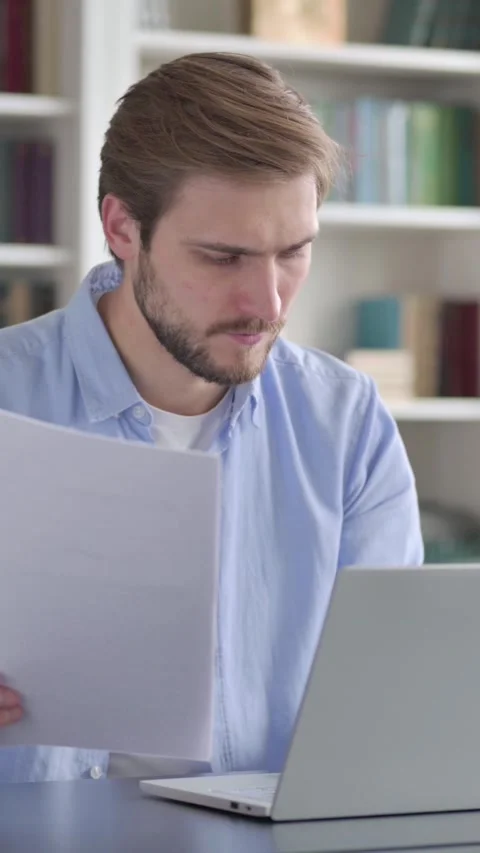 Man Reading Documents while using Laptop, Vertical Video Stock Footage 339578053