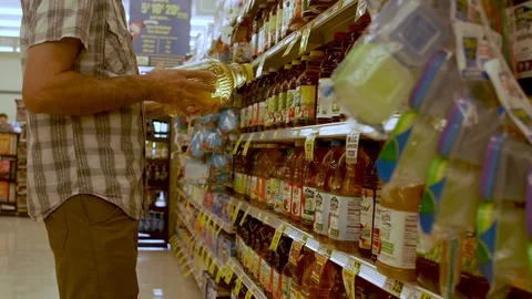 Man reading labels on various plastic juice bottles in a grocery store Stock Footage 120248943