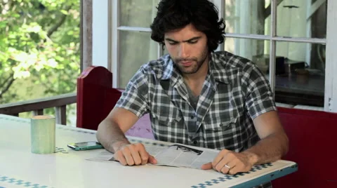 Man reading magazine, drinking coffee and answering cellphone Stock Footage 60949447