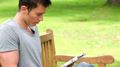 Man reading a newspaper while sitting on a park bench Vídeos de archivo 10816533