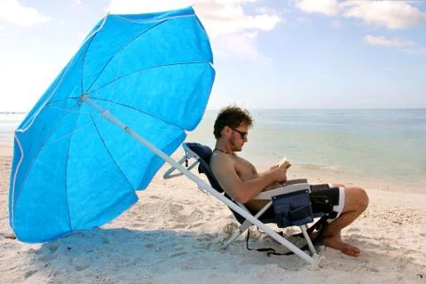 Man reading by ocean under beach umbrella Stock Photos