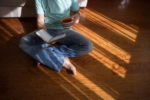 Man reading old hardback book holding in his hands, on the brown floor at home Stock Photos