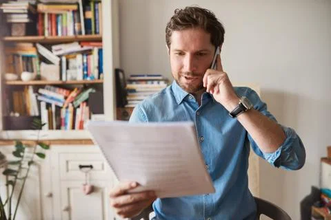 Man reading paperwork and talking on a cellphone at home Stock Photos