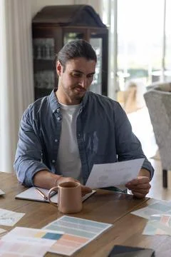 Man reading printed document with charts at wooden table at home, reviewing Stock Photos