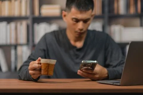 Man reading smartphone and drinking coffee in a library with bookshelf back.. Stock Photos