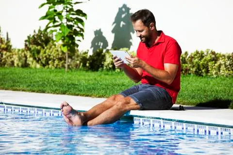 Man reading tablet sitting on the poolside. Stock Photos