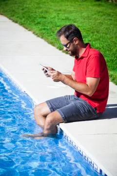 Man reading tablet sitting on the poolside. Stock Photos