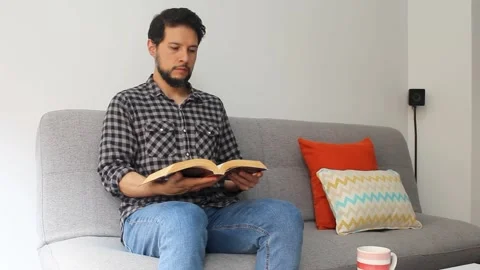 Man reading a text book sitting at the left side of a couch Vídeo Stock 340583402