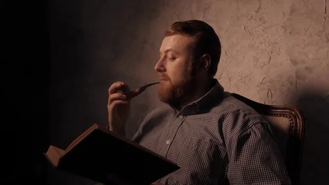 Man reads a book in a dark room and smoking pipe. 4K UHD 库存影片 73362745