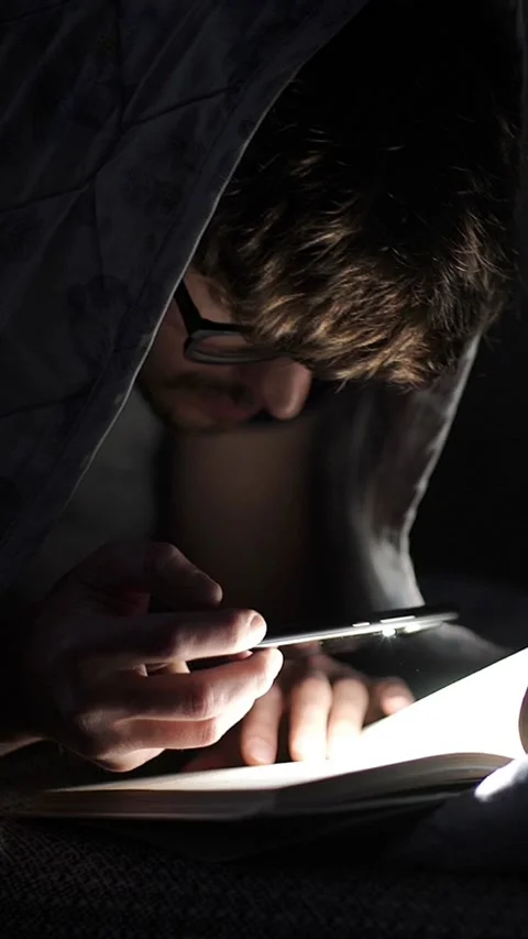 Man reads a book with a flashlight under the covers at night. Stock Footage 326634884