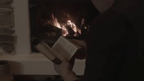 A man reads a book in front of a fireplace Stock Footage 74196261