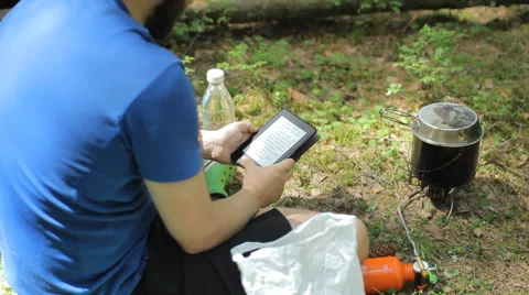 Man reads an e-book in the forest. Near the tourist pot on a gas burner Stock Footage 64529713