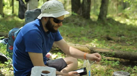 Man reads an e-book in the forest. Near the tourist pot on a gas burner Stock Footage 64530351