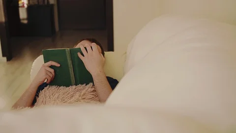 A man reads an old book while lying on a sofa Stock Footage 129892381