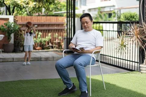 A man reads peacefully while a young girl holds a basketball in the backgro.. Stock Photos