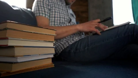 A man reads a thick book sitting on the couch at home, engaged in self-education Stock Footage 105800160