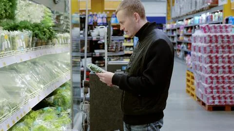 Man reads a vegetable label in a busy grocery store aisle, surrounded by fresh Foto stock