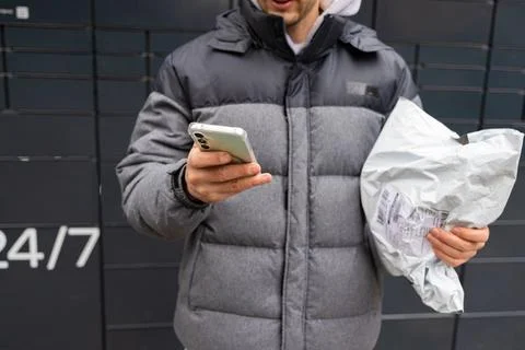Man receiving parcel from automatic post box using smartphone outdoors. Photos