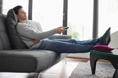 Man reclining on a couch and watching television Stock Photos