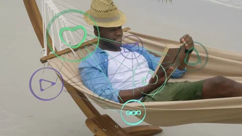 Man reclining in hammock on beach, tapping tablet to check social media icons Stock Footage 333975533