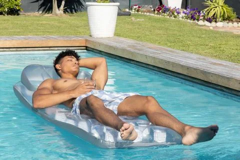 Man reclining on silver lounger in backyard pool wearing blue checkered trunks Foto stock