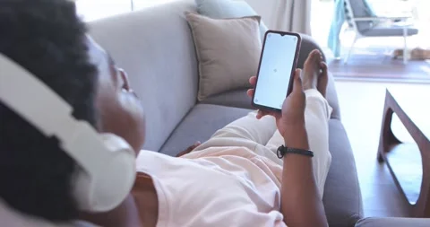 Man reclining on sofa at home wearing headset, tapping smartphone trying to Vídeos de archivo 340969464