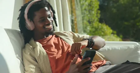 Man reclining on sofa, pink headset, music playing, tapping phone, waving and Stock Footage 342023499