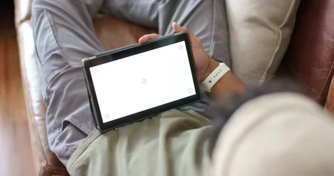 Man is reclining on sofa, tablet resting on lap while adjusting tilt to align Stock Footage 341932688