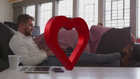 Man reclining on sofa typing on laptop pausing 3D heart appearing obscuring Stock Footage 333657247
