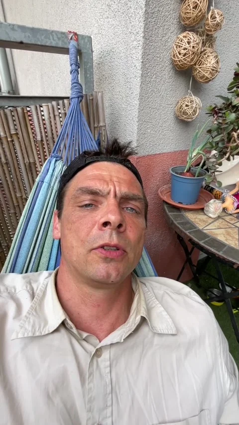 Man reclining in striped hammock on balcony with subtle head shift calm mood Stock Footage 344588472
