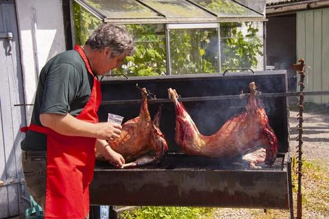 Man with red apron roasting two whole pigs slowly on a grill Stock Photos