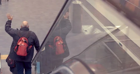 A man with a red backpack goes down the escalator and waves his hand  Stock Footage 119596365