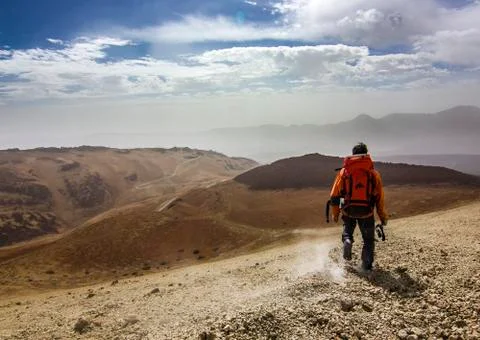 Man with red backpack on rocky path in desert Stock Photos