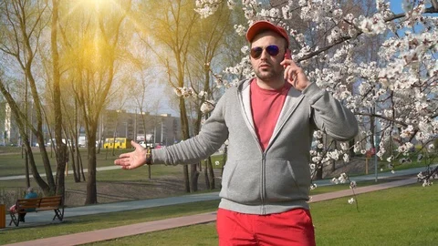 Man in red baseball cap in sunglasses talks on smartphone in the park Vídeo Stock 118716305