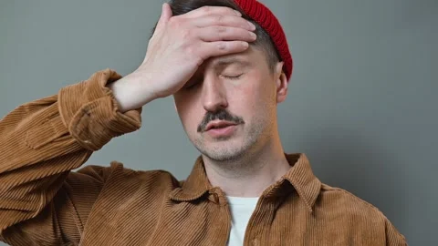 A man in a red beanie and brown jacket holds his forehead, displaying signs of Видео 337642454