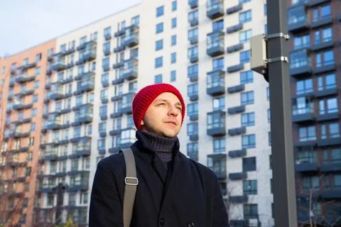 Man in red beanie standing in front of modern apartment building. Urban Stock Photos