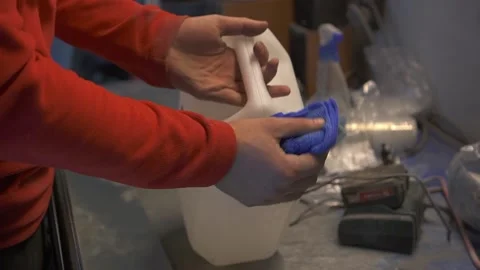 A man in red clothes in a workshop on a work table pours a solvent on a blue rag Vídeo Stock 134842398